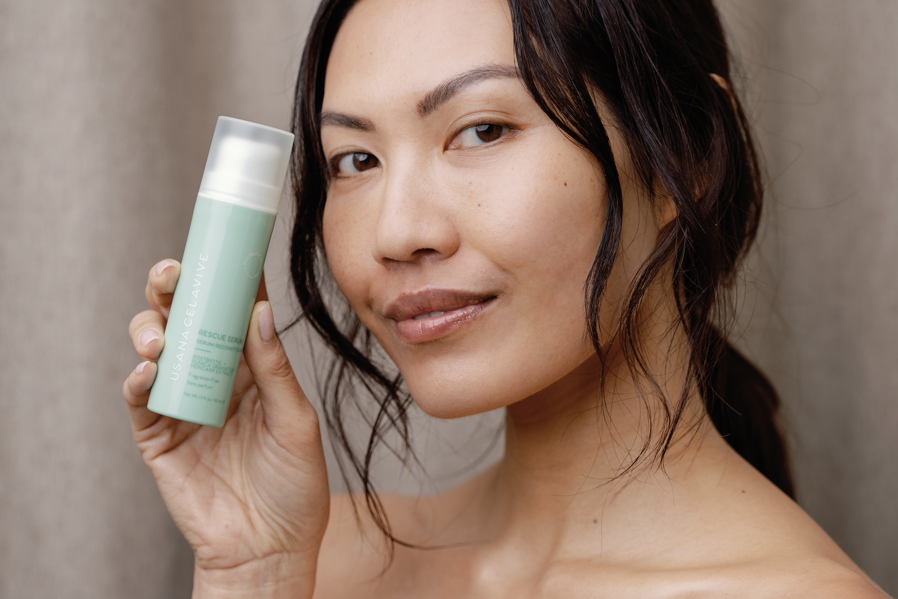 woman holding postbiotic skincare bottle to her face